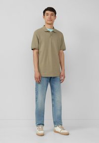 Olijf groene polo shirt, relaxte pasvorm, gecombineerd met lichtblauwe jeans. Schoenen hebben een wit en beige ontwerp met een gestructureerde zool.