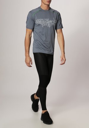 Camiseta deportiva gris con detalles verdes y gráfico de texto, combinada con mallas negras que presentan una textura hexagonal. Zapatillas negras.