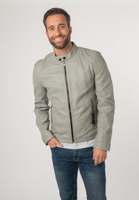 Grijze leren jas met een staande kraag, voorkantrits en zijzakken. Getextureerde afwerking met contrasterende zwarte ritsaccenten.