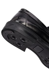 Zwarte lakleren schoen met een ronde neus en dikke zwarte rubberen zool. Heeft ronde inkepingen op de loopzool voor grip.
