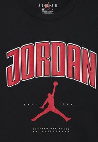 Must musta- ningmust  tekst terava punane "JORDAN" kiri ja graafika mängijast kes on õhus, koos jumpman logoga.