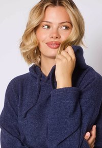 Marineblauwe fleece hoodie met een voorzak, een capuchon met trekkoord en geribde manchetten. Zachte textuur en een comfortabele pasvorm.