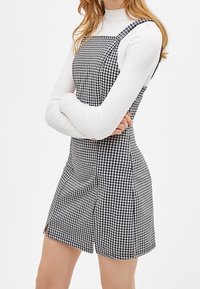 Svart och vit rutad klänning i gingham-stil med justerbara remmar, strukturerad tyg och en något utsvängd nederdel, tillsammans med en ribbad vit polokrage.