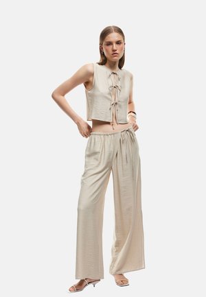 Beige crop top med detalj av framsidan och vida byxor. Slät, lättviktig tyg med avslappnad passform. Enkel design, minimala accenter.