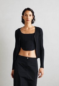 Chaqueta corta de canalé negra con mangas largas, acompañada de una blusa corta negra a juego. Tejido suave, diseño ajustado y estilo minimalista.