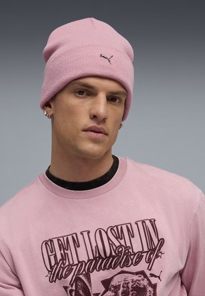 Light pink beanie with a ribbed texture and a small Puma logo. Worn with a matching pink graphic sweatshirt featuring dark print.