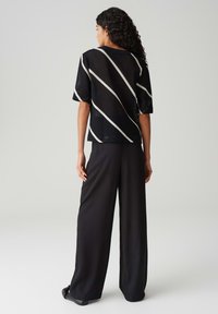 Top in rete nera con strisce diagonali bianche, abbinato a pantaloni neri a gamba larga. Il top presenta maniche corte e una vestibilità morbida.