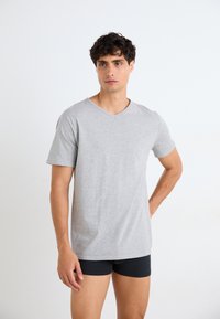 T-shirt en coton gris clair à col en V avec des manches courtes, présentant une coupe décontractée et une texture lisse, porté sur des boxers noirs.