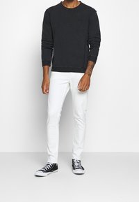 Felpa nera con colletto a girocollo e maniche lunghe, abbinata a jeans bianchi skinny e sneaker alte nere.