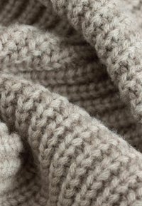 Strikket beige garn med en blød, tekstureret overflade. Stoffet viser et tykt vævemønster, der skaber et hyggeligt, kraftigt udseende.