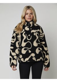 Pull en polaire noir et crème avec une fermeture éclair moitié, arborant un motif abstrait tourbillonnant et des manches longues. Texture douce et coupe décontractée.