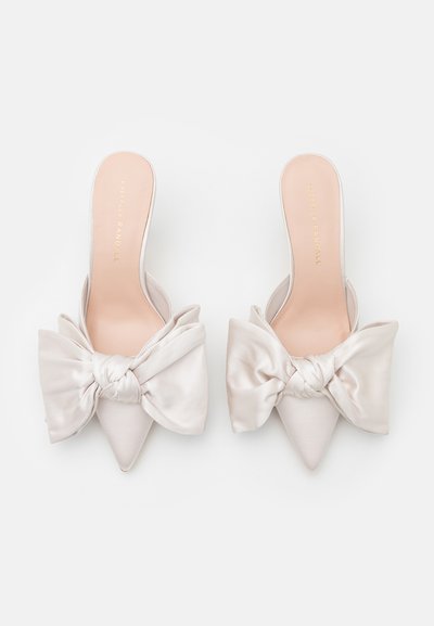Pointed-toe slip-on mules in soft beige satin with large knotted bows on each toe. Smooth texture and minimalistic design.