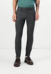 Pantalones de vestir gris oscuro con un sutil patrón de cuadros, con cierre de botón y corte ajustado, combinados con zapatos marrones de cordones.
