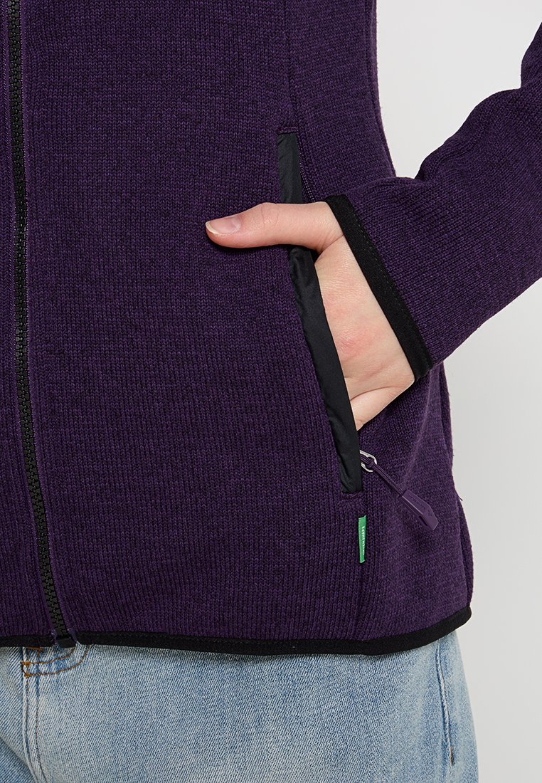 Lila Zip-Jacke mit gerippter Textur, schwarzem Besatz, seitlichen Taschen und einem grünen Akzent-Tag nahe dem Saum.