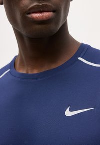 Gros plan sur une personne portant un maillot de sport Nike bleu avec un logo blanc sur la poitrine et une bande blanche sur l'épaule.