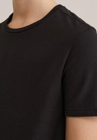 Černé bavlněné tričko s kulatým výstřihem, krátkými rukávy a hladkou texturou. Viditelné švy podél okrajů.