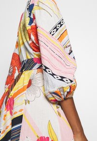 Robe multicolore avec des motifs floraux et rayés, manches courtes bouffantes et taille cintrée. Fabriquée en tissu léger avec des détails texturés.