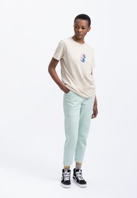 Beige katoenen t-shirt met een meerkleurig geometrisch ontwerp. Combinatie met mintgroene broek en zwarte high-top sneakers.