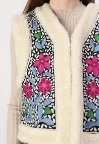 Cremfarbener Kunstfell-Weste mit lebhaftem Blumendruck in Pink, Blau und Grün auf schwarzem Hintergrund, weicher Textur und offenem Design.
