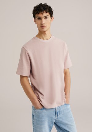 Light pink textured t-shirt with a crew neckline, short sleeves, relaxed fit, paired with light blue jeans.