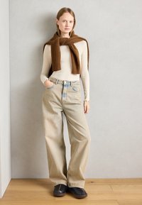 Beige wide-leg jeans, ribbed cream long-sleeve top, and a brown knit scarf. Black clogs with brown soles. Minimalist design against a light backdrop.