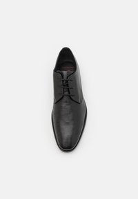 Scarpa da uomo in pelle nera con superficie testurizzata, punta rotonda e allacciatura con tre occhielli. L'interno presenta un'etichetta rossa per il comfort e la larghezza.
