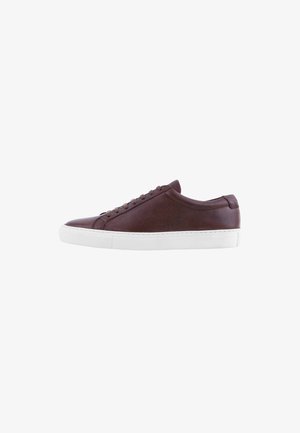 Brown leather sneaker with a smooth texture, rounded toe, white rubber sole, and seven eyelet lace-up design.