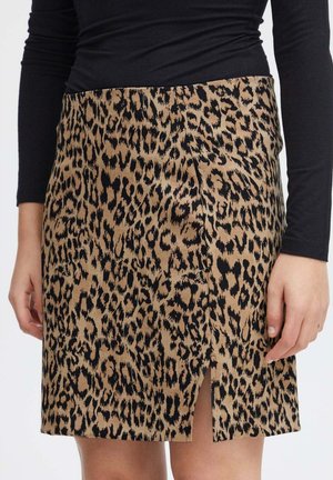 Kvinde iført nederdel med leopardprint i brune og sorte nuancer med frontslids, kombineret med en tætsiddende sort langærmet top.