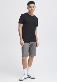 Fekete pamut póló, szürke, felgombolt ujjú rövidnadrág, fehér Nike zoknik, és szürke cipők fekete csíkokkal. Egyszerű dizájn, nincs látható minta.