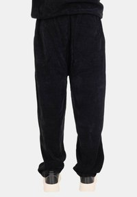 Pantaloni in corduroy neri con vestibilità comoda, dotati di tasche laterali e una texture liscia, abbinati a sneakers di colore chiaro.