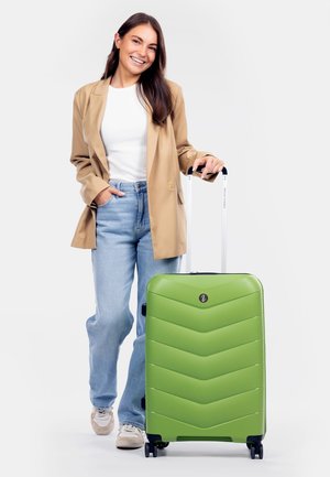 Valise rigide verte avec un design texturé en chevron, poignée rétractable, quatre roues et un logo noir à l'avant.