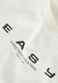 Biała bawełniana koszulka z odważnym czarnym napisem: "EASY STREETWEAR INDUSTRIES" oraz "34524.00001965", z okrągłym dekoltem i gładką fakturą.