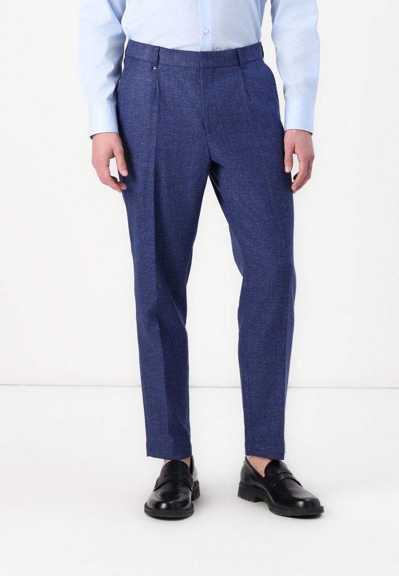 Blå texturerade byxor med veck, tillverkade av ett vävt tyg. Kombinerat med svarta skor, som visar en skräddarsydd passform och rak skärning.