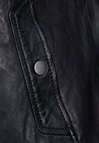 Zwarte leren jas met een close-up van een patchzak en een metalen drukknop, die de soepele textuur en gedetailleerde stiksels benadrukt.