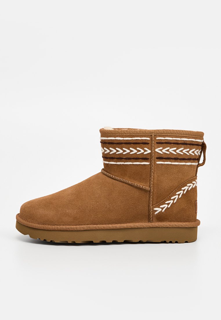 Stivale alla caviglia in scamosciato beige con cuciture decorative bianche. Presenta una punta arrotondata, un interno morbido e una suola in gomma piatta.