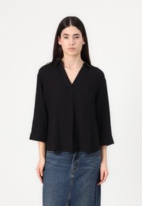 Black V-neck blouse with three-quarter sleeves, featuring a pleat detail at the center. Soft fabric and relaxed fit, worn over a denim skirt.