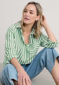Camicia a righe verdi e bianche con una vestibilità rilassata, abbinata a pantaloni in denim a gamba larga azzurri. Design semplice, tessuto casual.