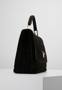 Czarna torebka zamszowa o wyraźnej strukturze, z złotym metalowym akcentem, górnym uchwytem, gładką fakturą i zapięciem na klapę.