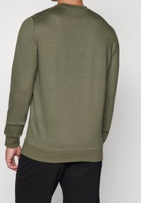 Sudadera verde oliva con cuello redondo, puños y dobladillo acanalados, con una textura suave y un ajuste cómodo. Diseño simple y minimalista.