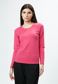 Langärmliges pinkes Oberteil aus weichem Stoff, mit rundem Ausschnitt und schlichtem Design, kombiniert mit dunklen Hosen.