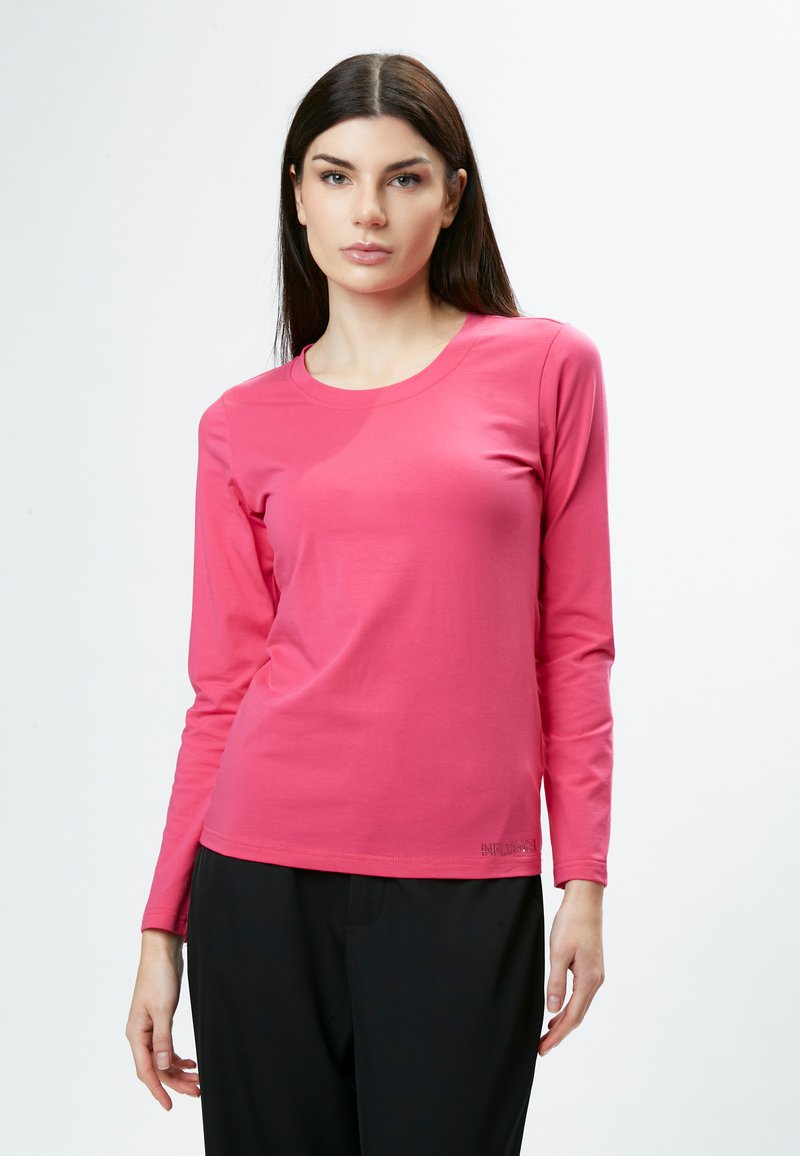 Langärmliges pinkes Oberteil aus weichem Stoff, mit rundem Ausschnitt und schlichtem Design, kombiniert mit dunklen Hosen.