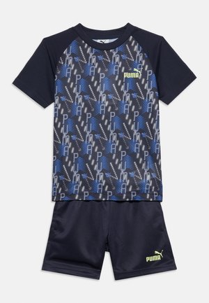 Completo sportivo per bambini Puma blu scuro con maglietta dal logo a motivo e pantaloncini tinta unita, entrambi con marchio Puma giallo sul petto e sulla gamba.