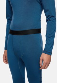 Maglia termica blu a maniche lunghe con fascia elastica nera in vita. Presenta cuciture piatte e una texture liscia. Adatta per essere indossata a strati.