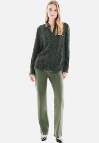 Chemise à manches longues vert foncé avec un col et un motif subtil, associée à un pantalon droit vert olive et des chaussures noires.