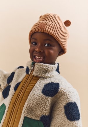 Brown ribbed beanie with ear accents; fleece jacket in cream with navy polka dots and green pockets; front zipper; warm and textured.