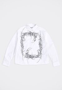 Λευκό πουκάμισο με μακριά μανίκια και κουμπιά, με μαύρο αφηρημένο σχέδιο αγκαθωτού τύπου που σχηματίζει ορθογώνιο πλαίσιο στην μπροστινή πλευρά.