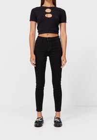 Zwarte geribbelde crop top met twee ronde uitsneden, gecombineerd met strakkere zwarte hoge taille spijkerbroeken en zwarte loafers met metalen accenten.