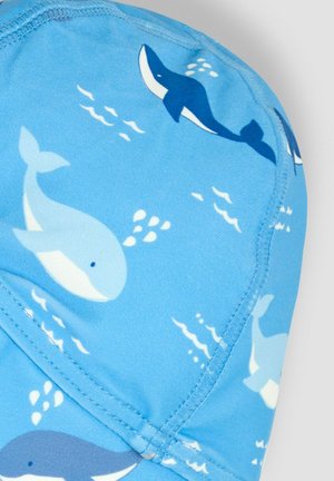 Blue swim cap featuring a pattern of white and dark blue whales, with small water splashes. Made from smooth, stretchy material.