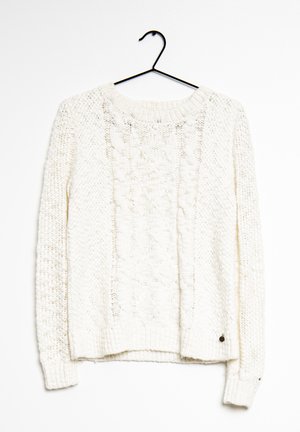 Weißer Strickpullover mit einer strukturierten Zopfmuster-Optik, rundem Ausschnitt, langen Ärmeln und geripptem Saum. Hängt an einem schwarzen Haken.