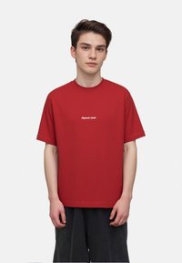Red cotton t-shirt with a relaxed fit, short sleeves, and a crew neck. Features white text "Original Classics" on the front.